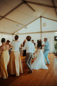 Personnes de différents âges dansant joyeusement sur un parquet en bois sous une tente blanche décorée de lanternes.
