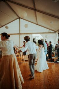 Des gens dansent joyeusement sur un parquet en bois sous une tente décorée de lanternes, avec un groupe de musique en arrière-plan.